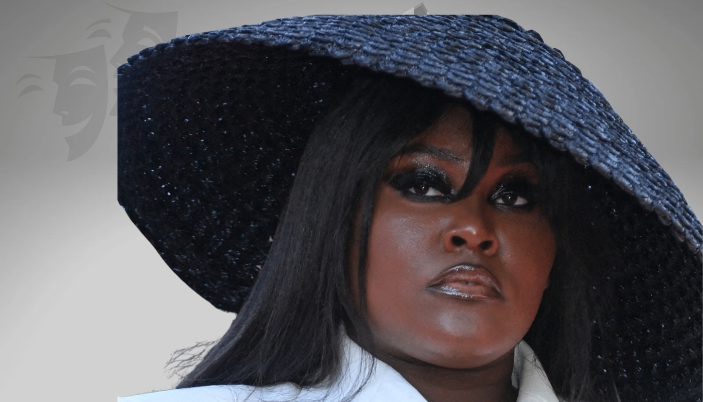 Yseult wearing a large black hat, showcasing bold eye makeup and a confident expression