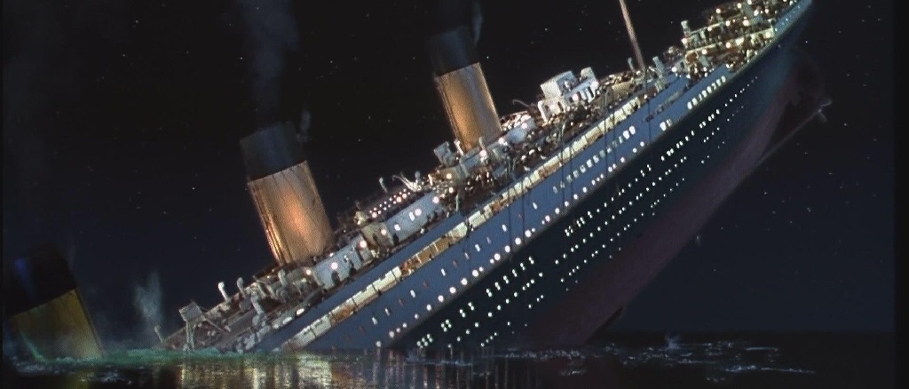 The RMS Titanic tilting vertically into the ocean at night, with lights still glowing and smoke rising from the funnels as it begins to sink