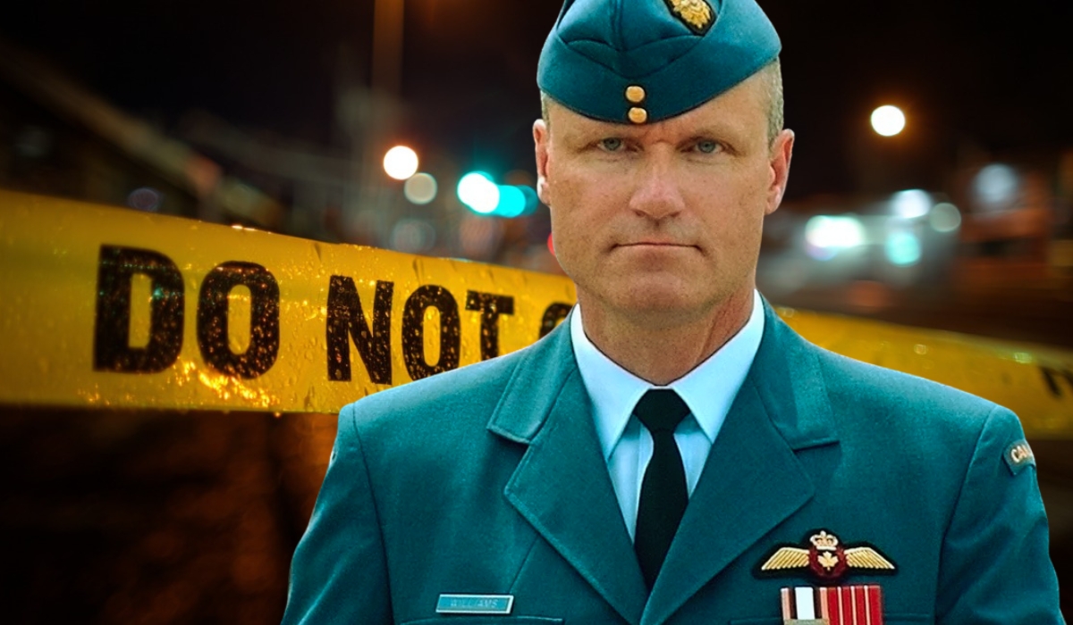 A man in a military uniform stands in front of yellow police crime scene tape with the words “DO NOT CROSS” at night